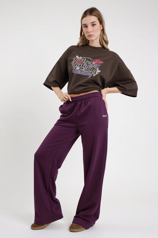 Pantalone Wide Leg SMX Limited Edition viola melanzana 65% cotone french terry vita elastica alta logo SMX bianco coscia laterale gamba larghissima palazzo frontale intera mani fianchi - modella intera frontale mani fianchi sguardo frontale capelli castani chiari sfondo bianco t-shirt crop cioccolato grafica abbinata