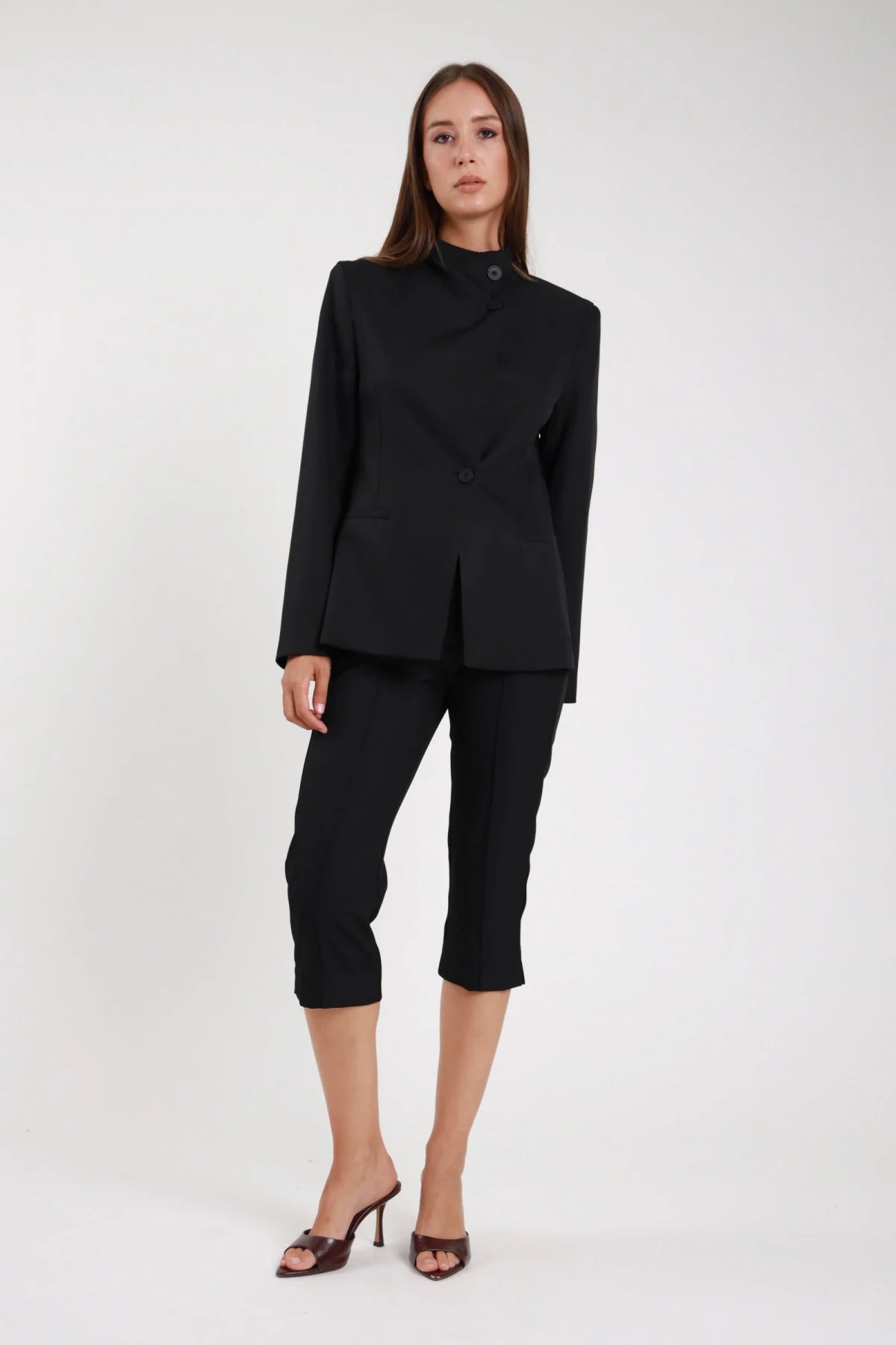 Pantaloni capri pinocchietto nero tessuto stretch vita alta fascia strutturata - modella frontale intera mano sul petto sguardo frontale sandali neri tacco capelli castani lisci
