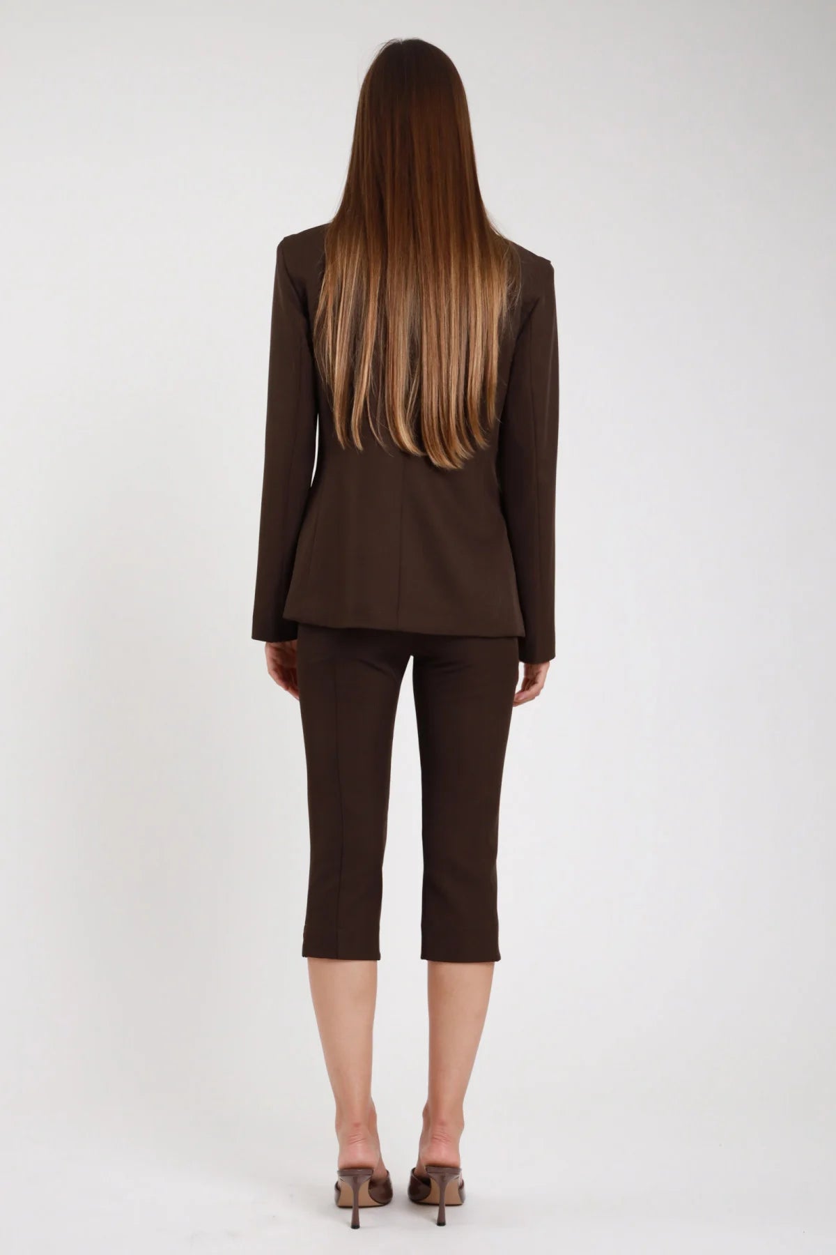 Pantaloni capri pinocchietto cioccolato marrone scuro retro gamba sigaretta spacco - modella retro intera tacchi marroni capelli castani lisci lunghi