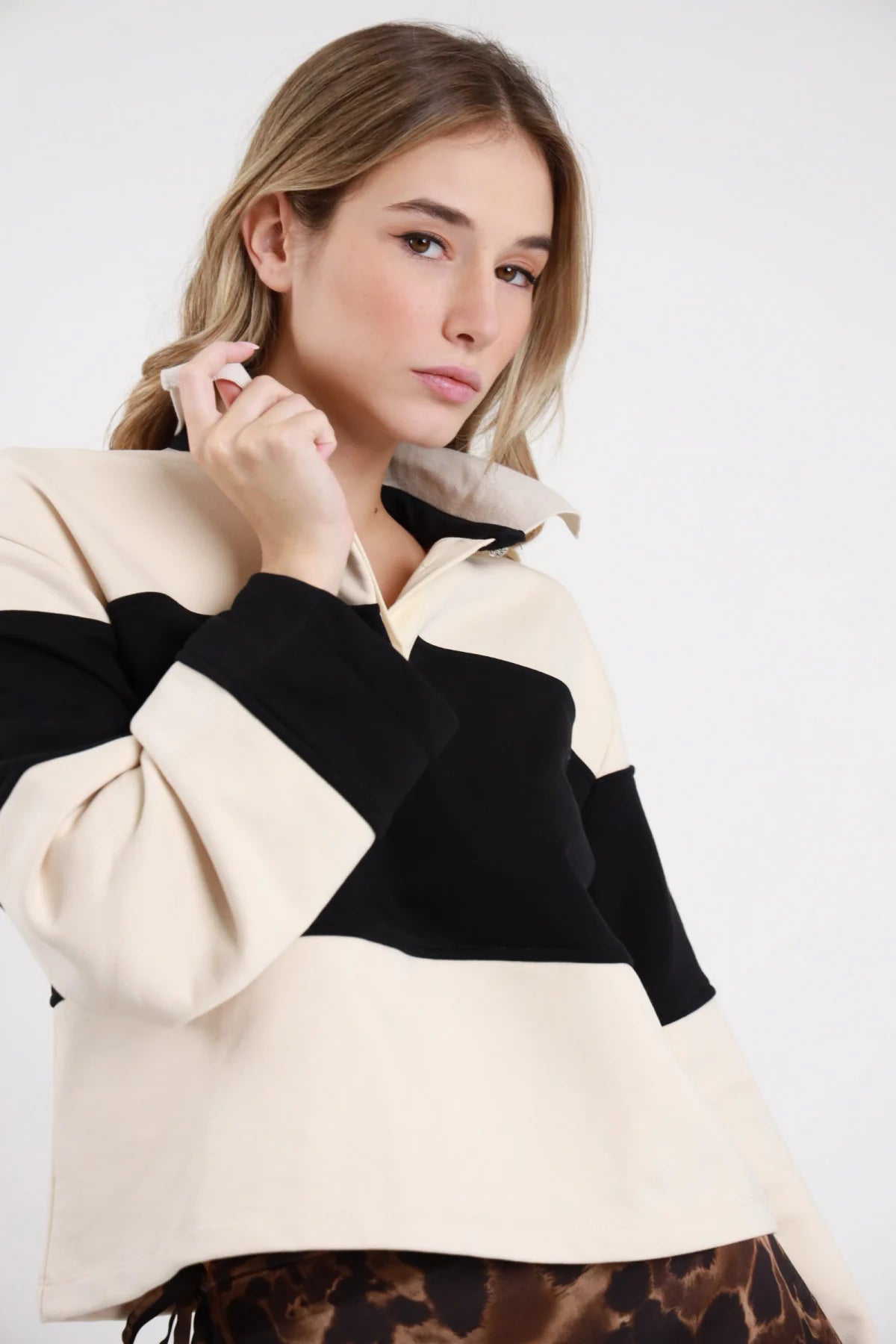 Polo Felpa Righe panna avorio nero 65% cotone colletto polo zip bottone dorato gioiello dettaglio fasce color block panna nero busto 3/4 mano colletto - modella busto 3/4 mano colletto sguardo intenso 3/4 capelli biondi mossi sfondo bianco minigonna animalier frange abbinata