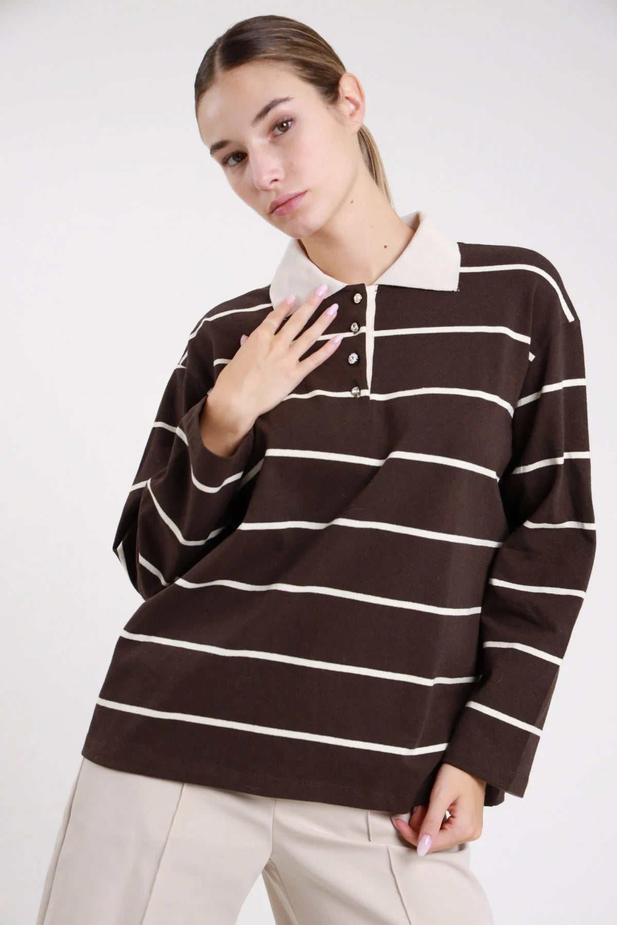 Polo righe rugby cioccolato panna frontale busto mano petto colletto polo panna strutturato bottoni snap - modella frontale busto mano petto sguardo frontale pantaloni beige capelli castani lisci