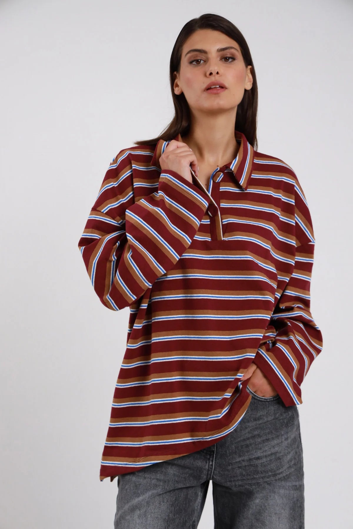 Polo Oversize Rugby Righe Multicolor bordeaux marrone cammello righe sottili blu elettrico bianco celeste 77% cotone colletto polo rovesciato ampio bottone collo manica ampia drop batwing silhouette maxi boxy fondo dritto asimmetrico frontale - modella busto 3/4 frontale posa mano colletto sguardo frontale intenso capelli castani lisci sfondo bianco jeans grigio antracite