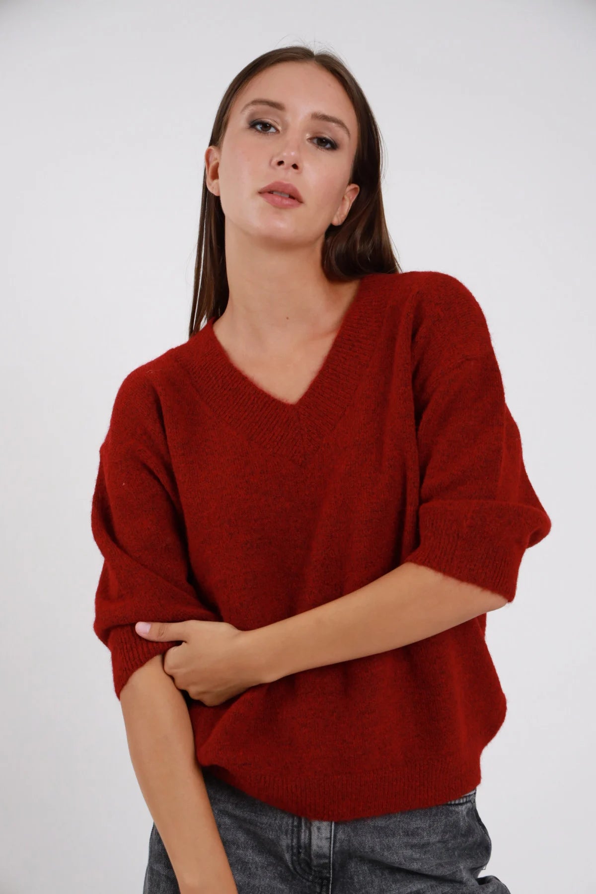 Pullover Scollo V rosso mattone bordeaux maglia ultra morbida scollo V ampio manica 3/4 balloon risvolto orlo coste oversize boxy busto frontale 3/4 braccia incrociate sguardo laterale - modella busto frontale 3/4 braccia incrociate sguardo laterale capelli castani sfondo bianco jeans grigi