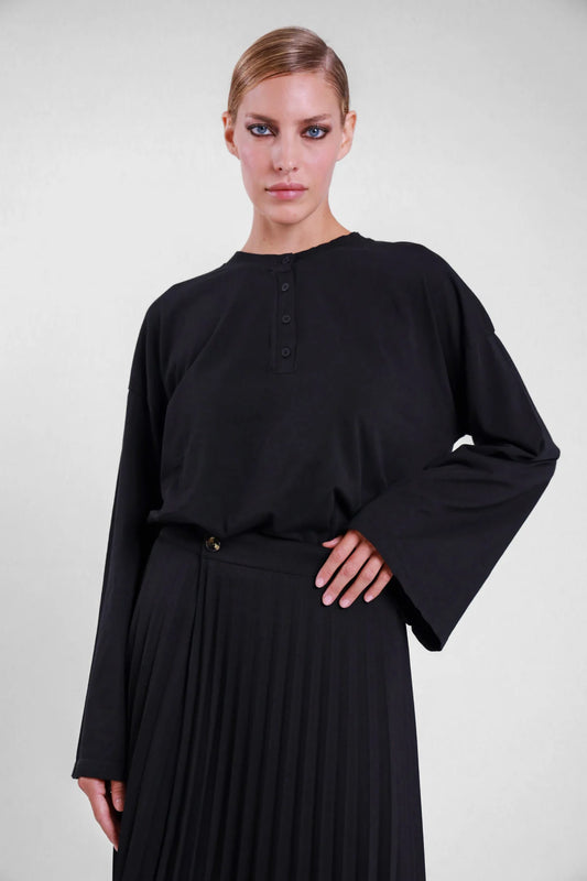 T-shirt Susy Mix nera con maniche lunghe a campana e scollo serafino, indossata con gonna plissé