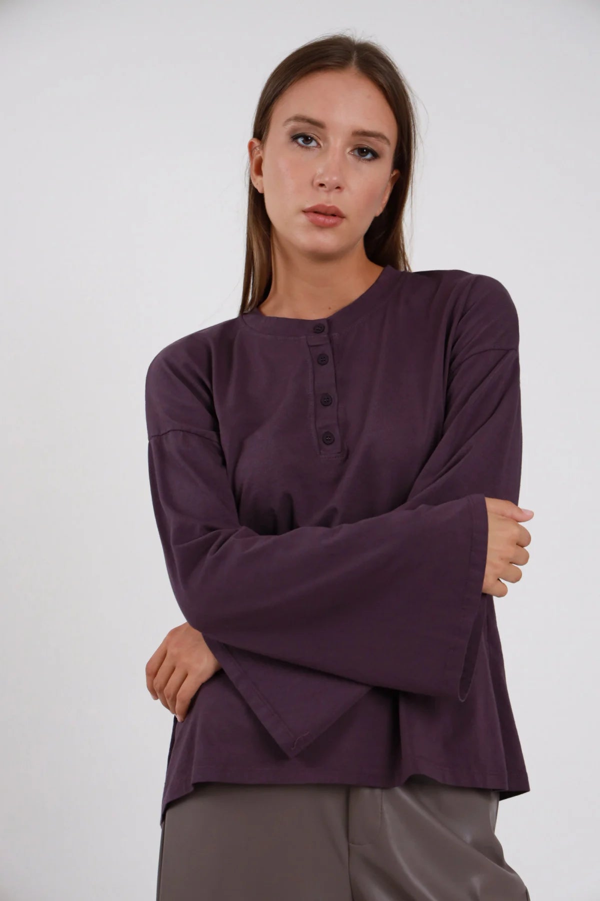 T-shirt Susy Mix viola con scollo serafino e maniche svasate, indossata con pantaloni