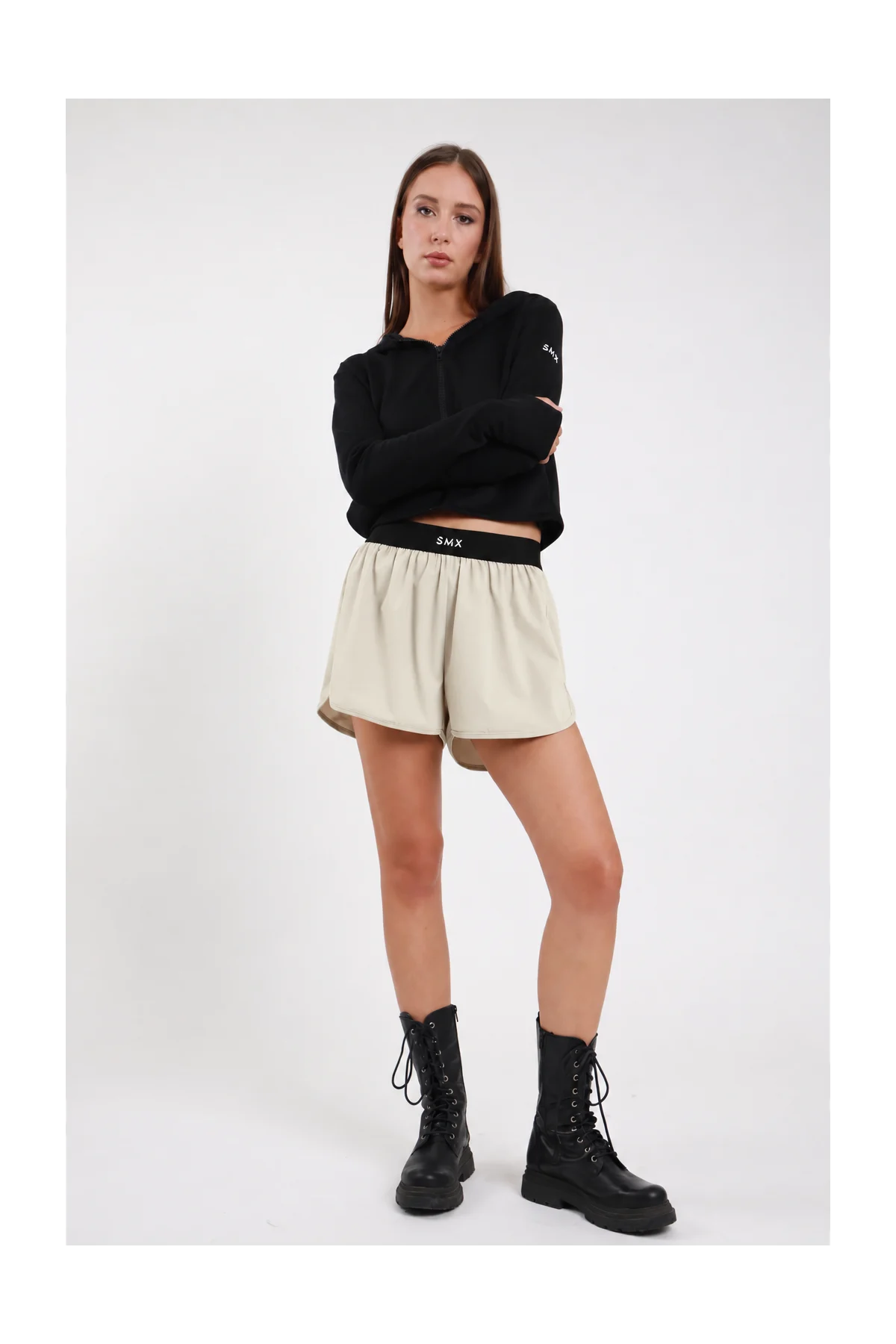 Short Soft Air Skort DAYTHRU sabbia beige chiaro elastico nero logo SMX bianco gonna sovrapposta arricciata fluida silhouette skort frontale intera posa statica braccia incrociate sguardo frontale - modella frontale intera posa statica braccia incrociate sguardo frontale capelli castani lisci sfondo bianco felpa crop zip nera coordinata stivali combat neri