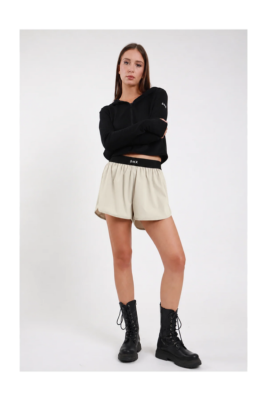 Short Soft Air Skort DAYTHRU sabbia beige chiaro elastico nero logo SMX bianco gonna sovrapposta arricciata fluida silhouette skort frontale intera posa statica braccia incrociate sguardo frontale - modella frontale intera posa statica braccia incrociate sguardo frontale capelli castani lisci sfondo bianco felpa crop zip nera coordinata stivali combat neri