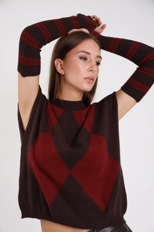Pullover smanicato manicotti argyle nero panna frontale busto braccio alzato cut-out spalla rombi maxi - modella frontale busto braccio alzato sguardo basso jeans grigio capelli biondi ondulati