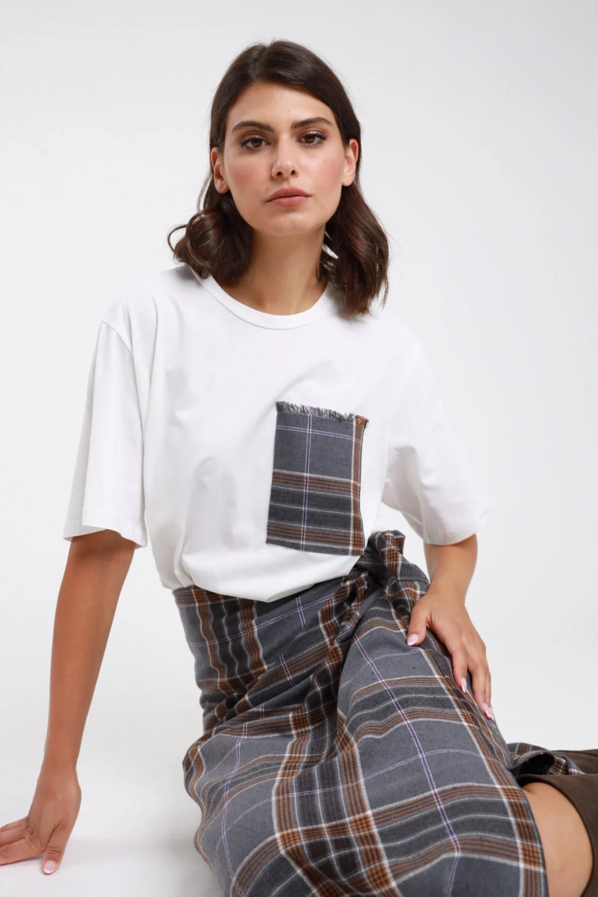 T-shirt oversize bianca con taschina check grigia - modella seduta, vista frontale