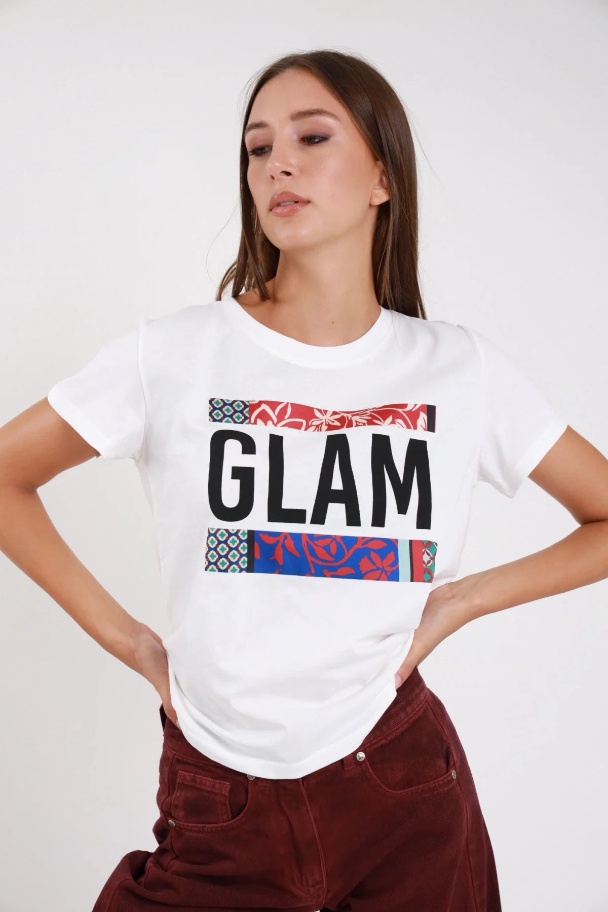 T-shirt glam bianca frontale mani fianchi stampa glam font bold bande patchwork geometrico floreale rosso turchese - modella frontale mani fianchi sguardo laterale basso pantaloni borgogna velluto capelli castani lisci