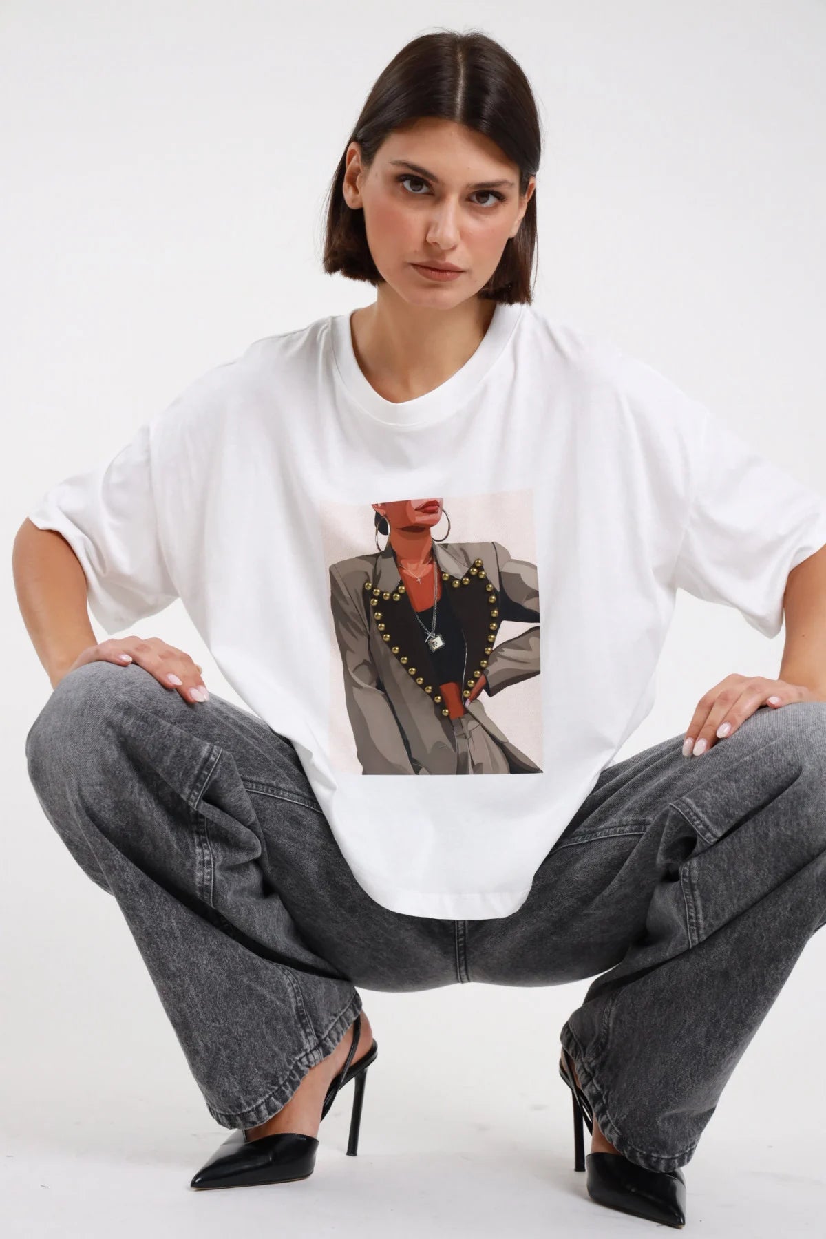 T-shirt stampa Susy Mix bianca a maniche corte ampie, indossata con jeans da modella accovacciata