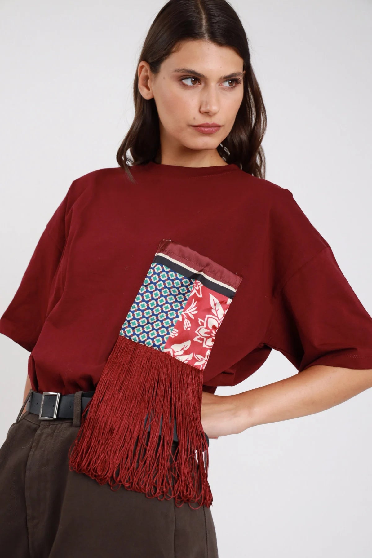 T-shirt bianca oversize boxy cropped taschina applicata patchwork seta raso multicolor righe bordeaux panna nero patch floreale rosso blu nero patch geometric tile blu verde bianco frange lunghe bordeaux rosso mattone pendenti girocollo manica corta drop shoulder frontale busto sguardo frontale gonna nera plissettata - modella frontale busto sguardo frontale intenso con gonna nera plissettata capelli castani scuri lisci sfondo bianco