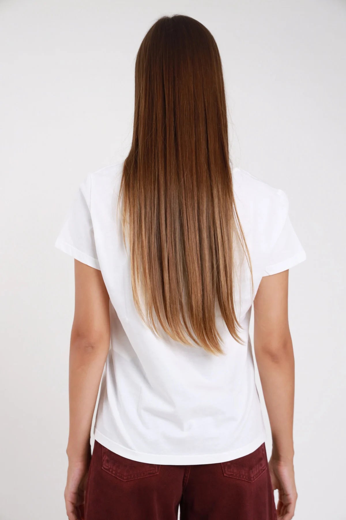 T-shirt glam bianca retro intera manica corta cuff orlo curvo corpo regular semi-fitted lunghezza vita fianchi - modella retro intera sguardo posteriore capelli lunghi castani lisci biondi ombre pantaloni borgogna velluto