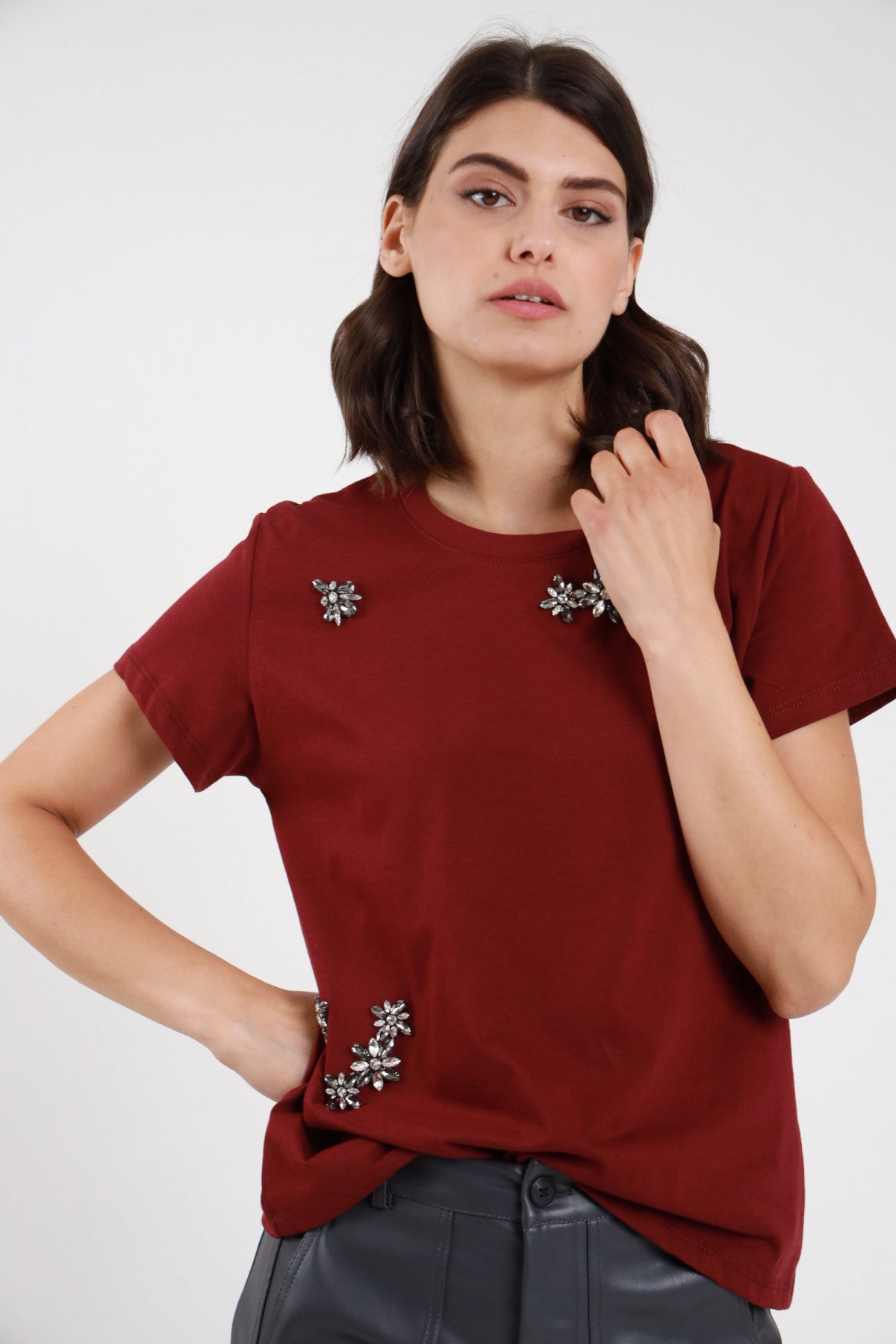 T-shirt strass bordeaux donna boxy con applicazioni fiori strass sparsi - vista frontale mano al collo con pantaloni in ecopelle grigi