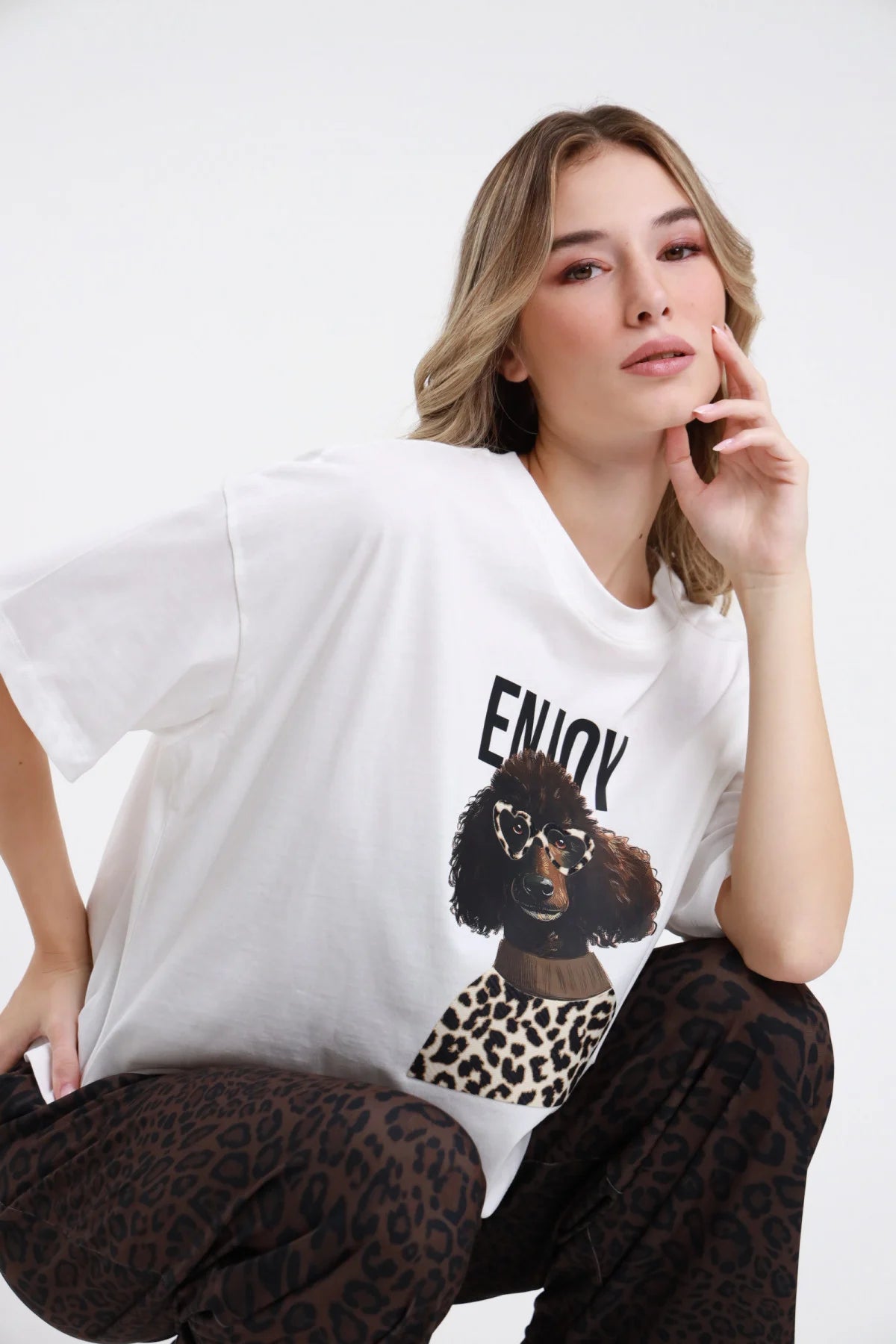 T-shirt Enjoy bianca da donna dalla linea morbida con stampa cagnolino e dettaglio animalier, indossata da modella seduta