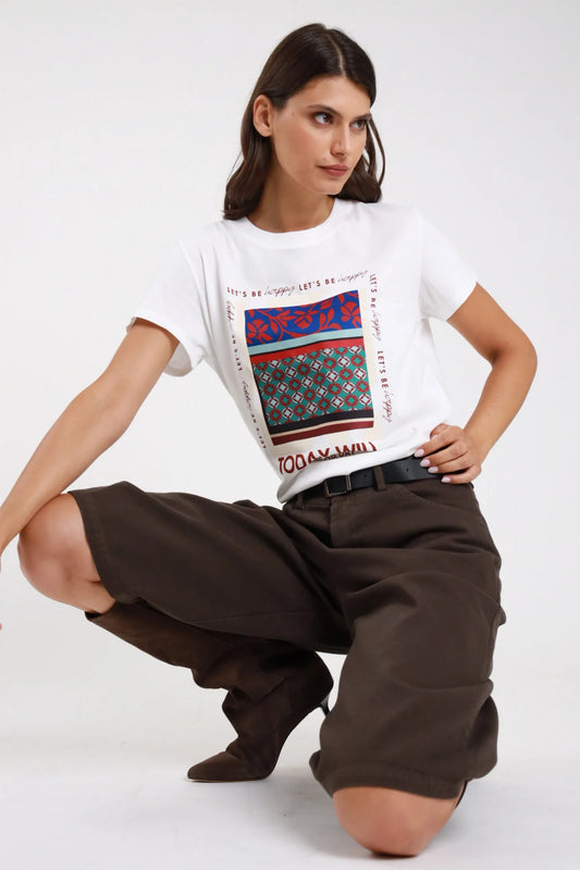 T-shirt bianca stampa grafica frontale art-poster patchwork ethnic tile multicolor blu elettrico rosso carminio verde teal bordeaux scritta Let's be happy bordo riquadro TODAY WILL BE A GOOD DAY smile frontale intera accovacciata dinamica - modella frontale intera accovacciata mano fianco sguardo laterale pantaloni marroni scuri stivali bassi marroni cintura nera sfondo bianco grigio