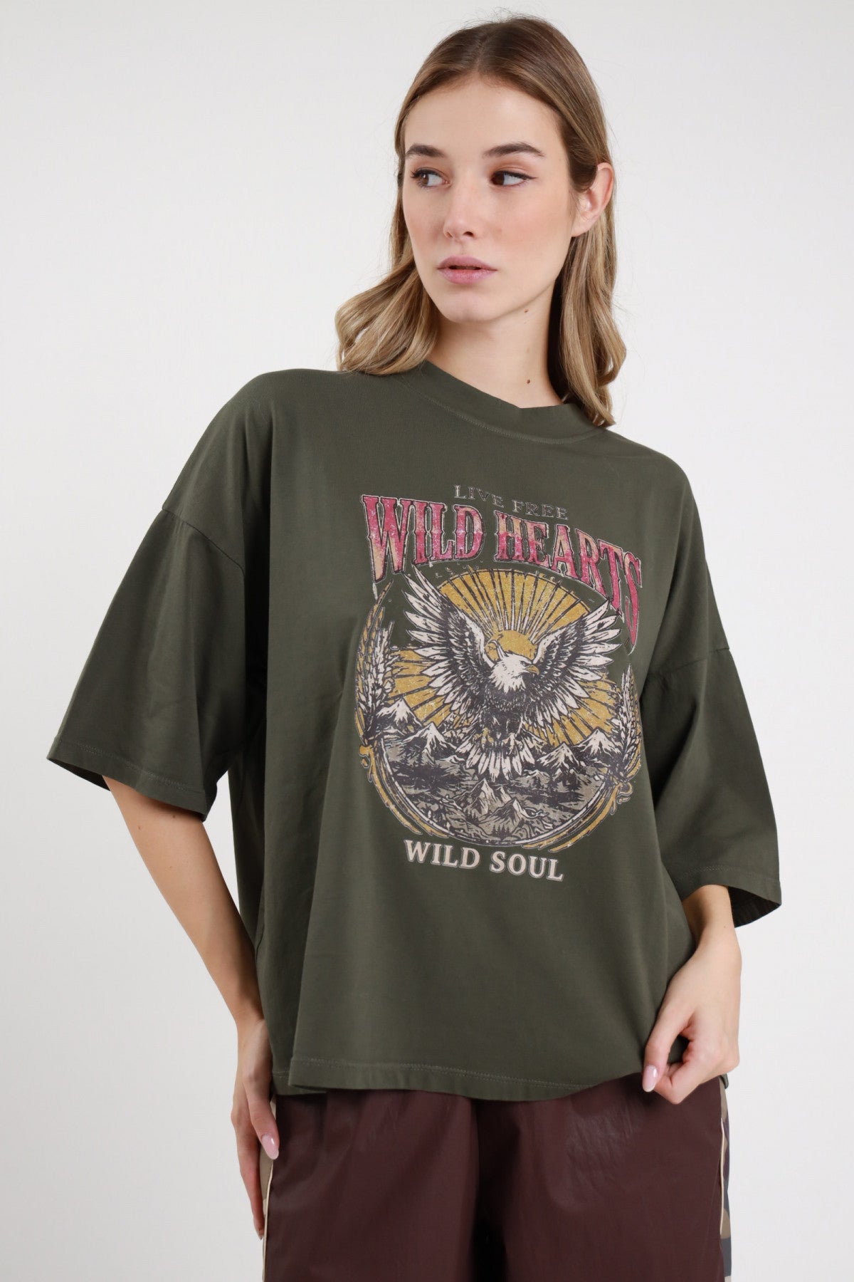 T-shirt Aquila verde militare oliva 95% cotone oversize boxy girocollo drop shoulder stampa grafica aquila americana Wild Hearts Wild Soul vintage western frontale busto sguardo laterale - modella busto frontale sguardo laterale capelli biondi ondulati sfondo bianco pantalone bande cioccolato abbinato