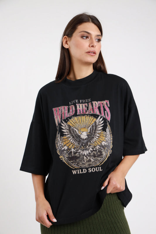 T-shirt Aquila nera 95% cotone oversize boxy girocollo drop shoulder stampa grafica aquila americana Wild Hearts Wild Soul vintage western frontale busto 3/4 - modella busto 3/4 sguardo laterale capelli castani scuri lisci sfondo bianco gonna maglia costine verde militare abbinata