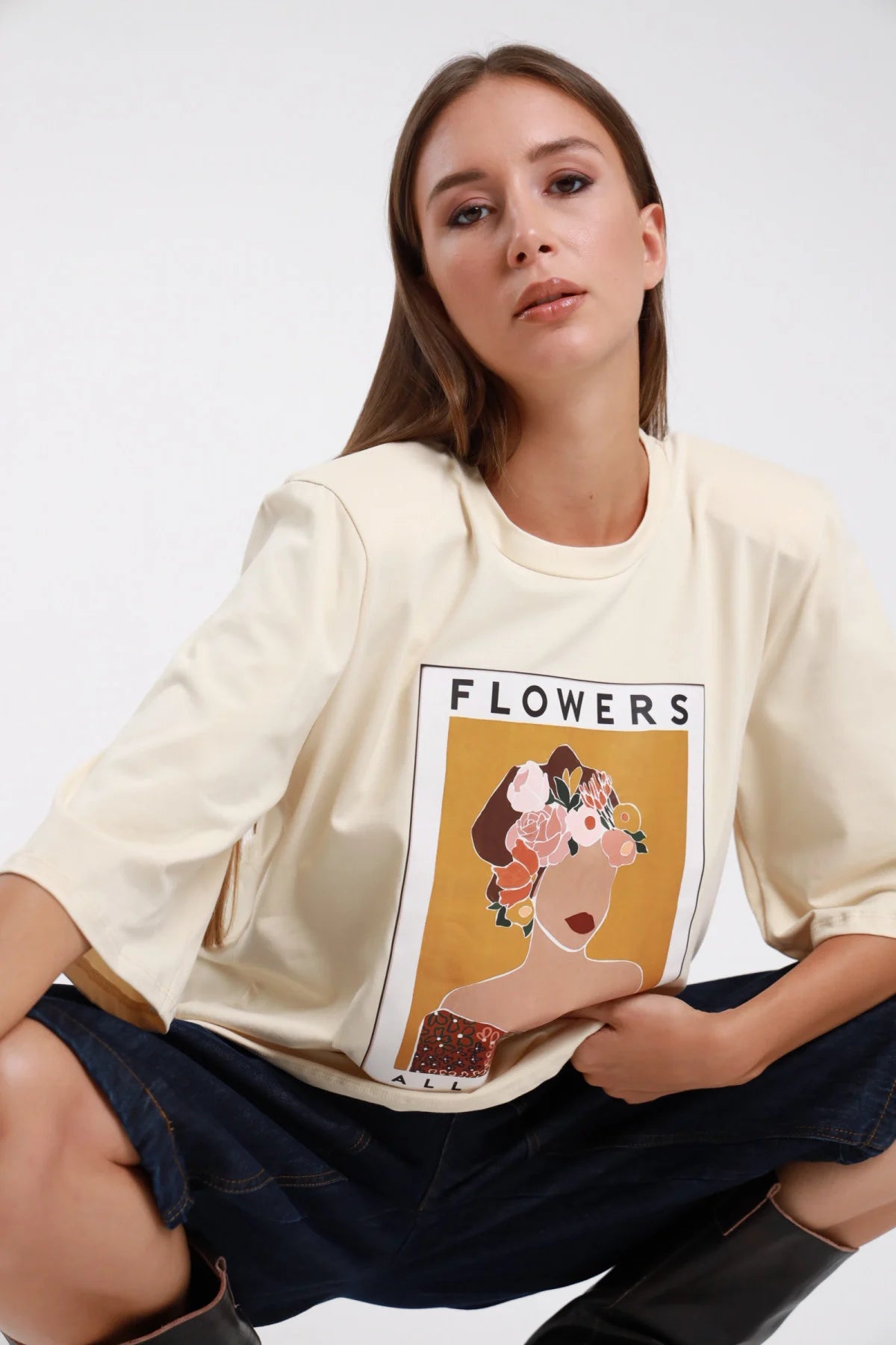 T-shirt Flowers All Around panna avorio oversize seduta stampa grafica artistica donna fiori - modella seduta jeans scuri stivali marroni sguardo frontale capelli castani lisci