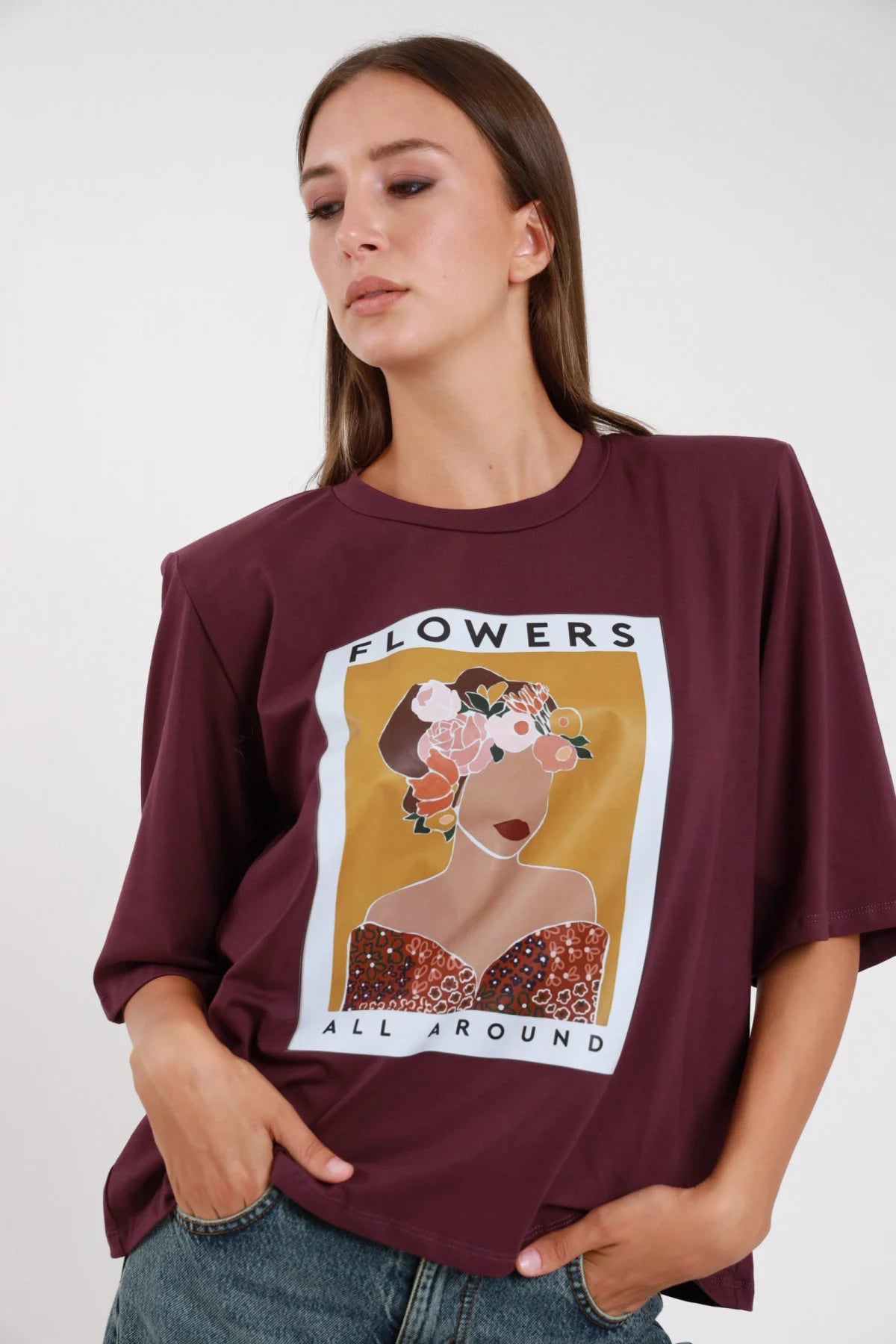 T-shirt Flowers All Around bordeaux prugna stampa grafica ocra fiori oversize - modella frontale intera mani in tasca sguardo basso jeans chiari capelli castani lisci