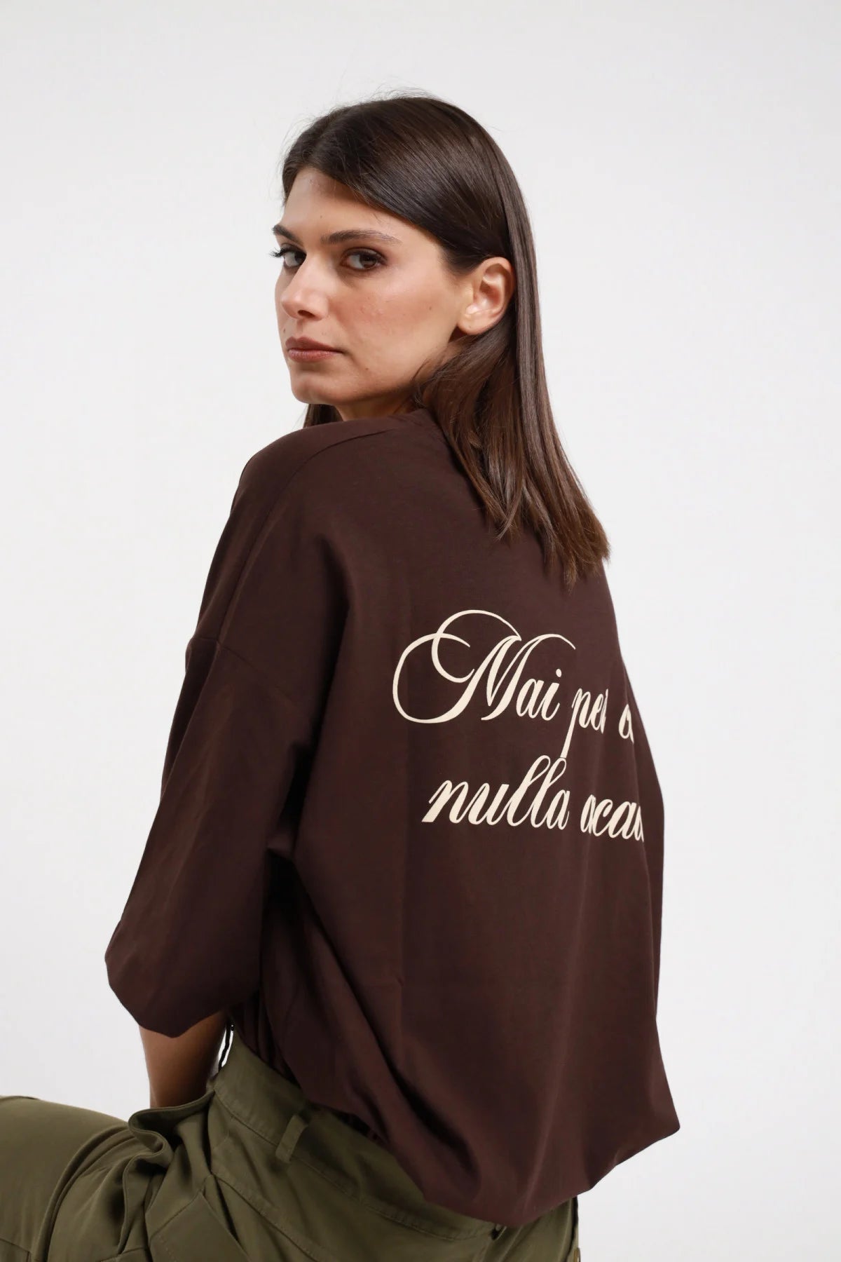 T-shirt over Mai per caso nulla accade Susy Mix Pre-Fall marrone cioccolato 100% cotone scritta corsivo panna retro 3/4 laterale sguardo camera - modella 3/4 laterale sguardo camera capelli scuri lisci sfondo bianco scritta corsivo retro parzialmente visibile pantaloni cargo verde militare abbinati