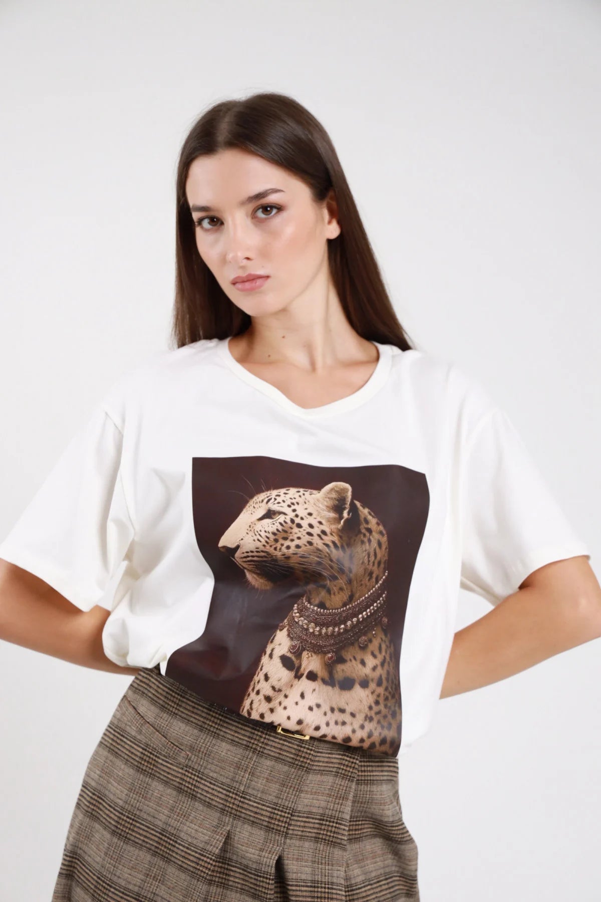 T-shirt stampa fotografica artistica leopardo profilo collana etnica gioiello oro bronzo marrone sfondo bruciato scuro bianco panna jersey frontale busto mani fianchi girocollo tondo manica corta balloon dolman corpo oversize boxy - modella frontale busto mani fianchi sguardo frontale intenso capelli castani scuri lisci sfondo bianco gonna check beige kaki cintura nera fibbia dorata