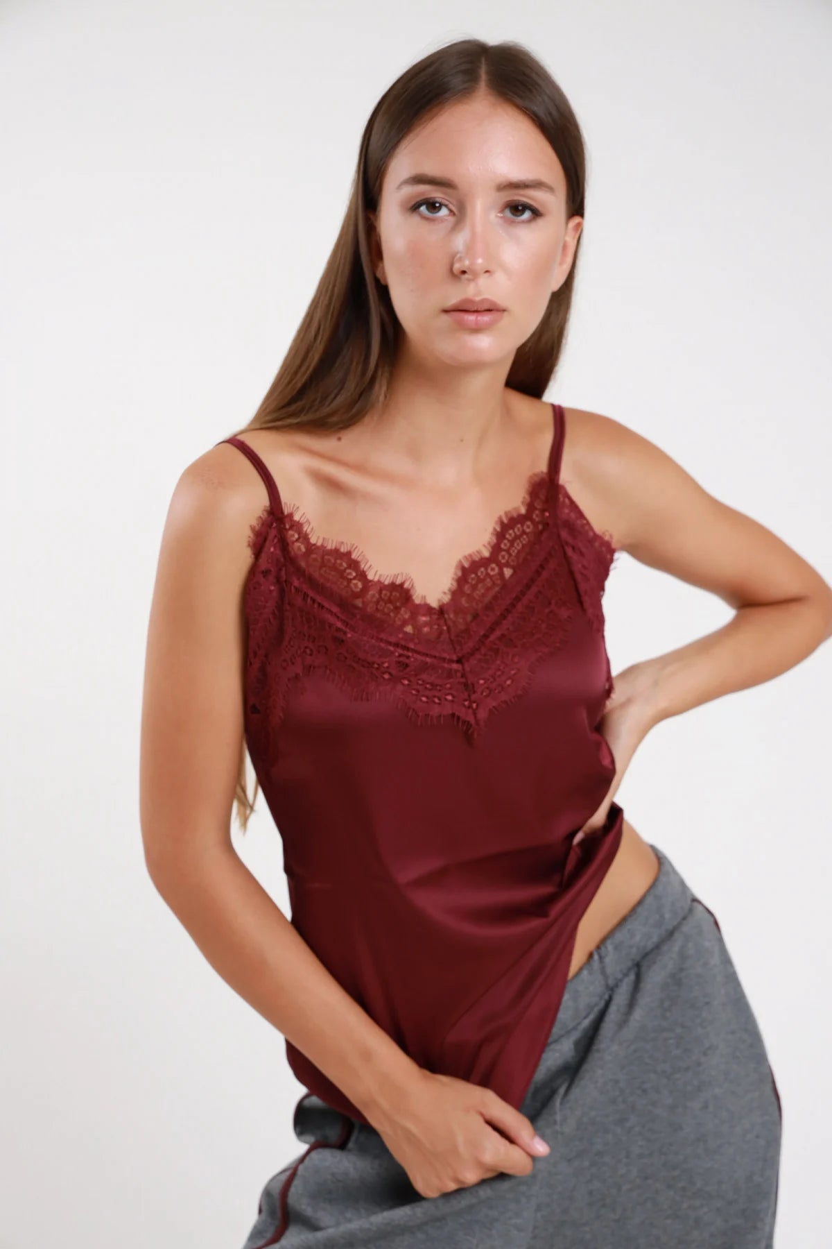 Top pizzo raso verde oliva scollatura V pizzo chantilly khaki scuro spalline sottili regolabili corpo fluido braccia conserte - modella frontale busto braccia conserte sguardo laterale alto pantaloni neri ecopelle capelli castani lisci