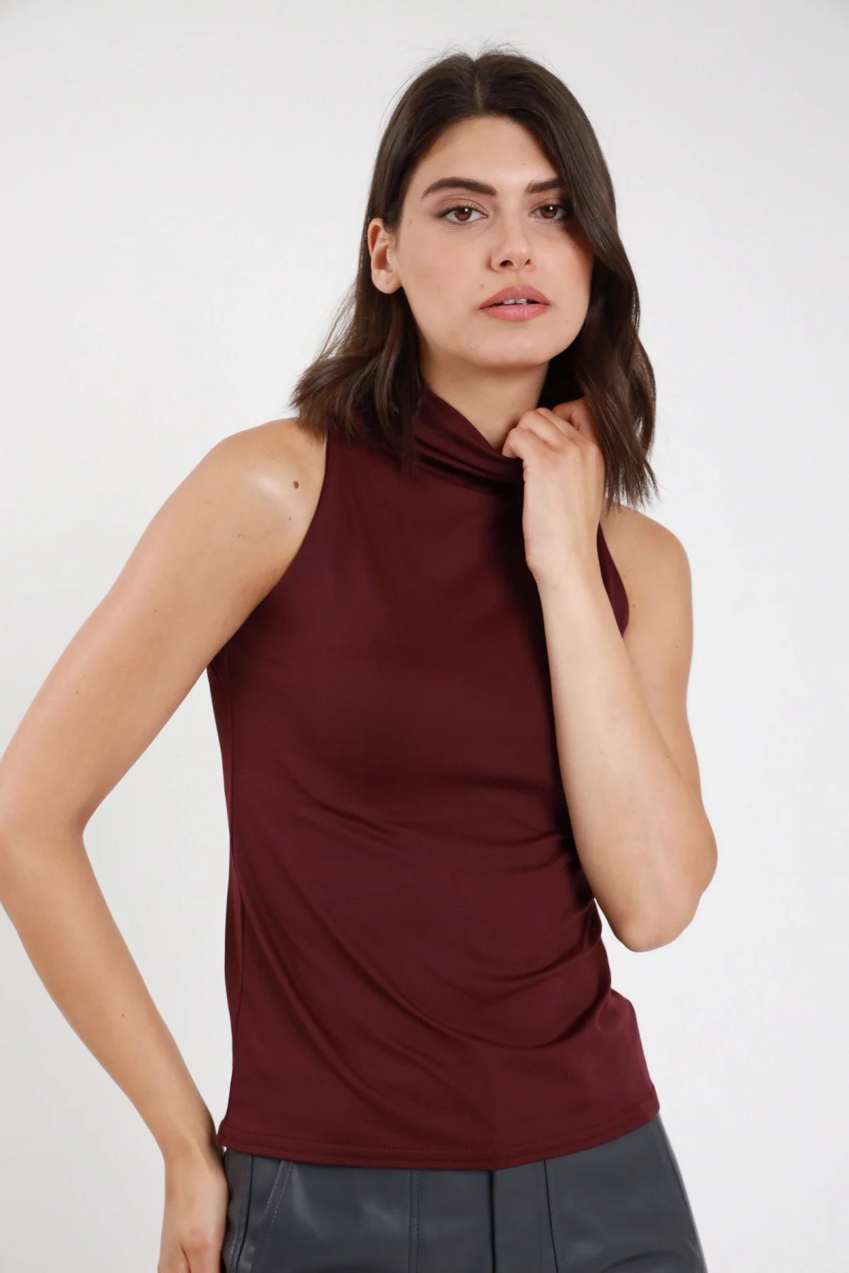 Top tactel bordeaux vinaccia donna collo alto arricciato drappeggio asimmetrico schiena halter - vista frontale mano al collo con pantaloni in ecopelle grigi