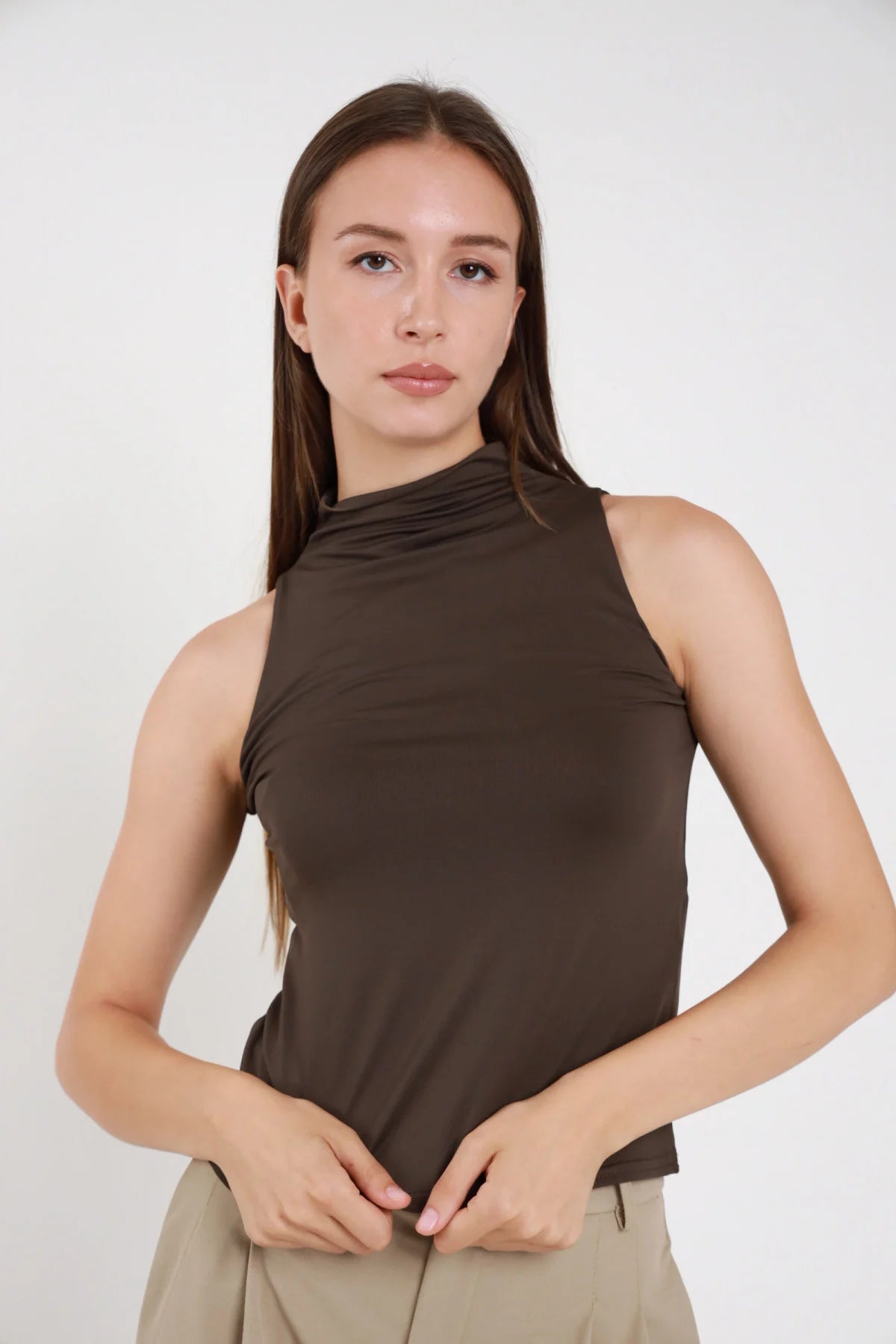 Top tactel marrone scuro donna collo alto arricciato drappeggio asimmetrico schiena halter aderente - vista frontale mani al ventre con pantaloni beige